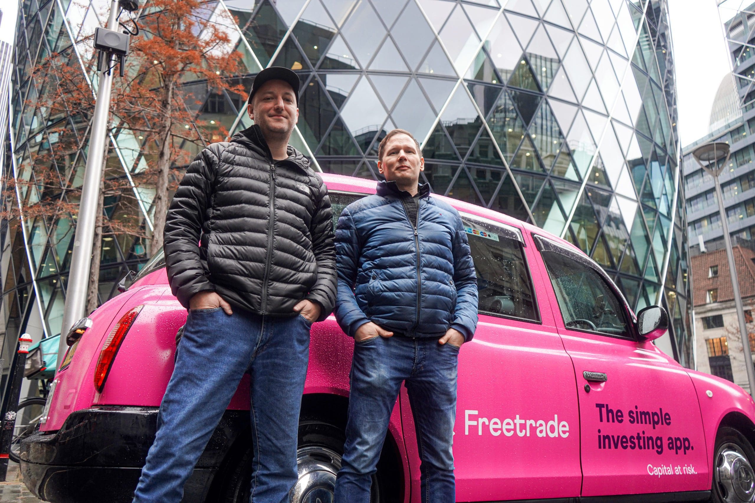Two men standing in front of a pink taxi 